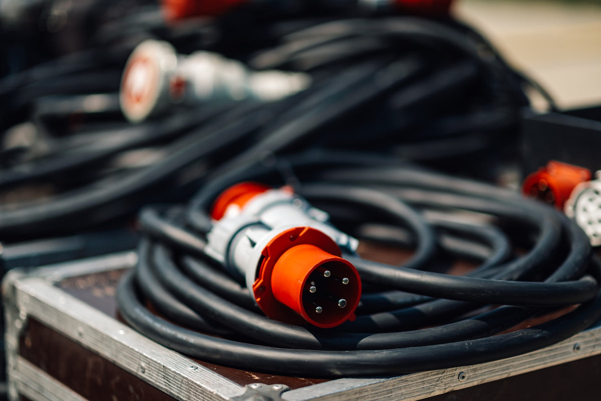 Close-up of L14‑30 and L5‑30 twist‑lock connectors on heavy‑duty generator cords powering a home transfer switch and an RV in a driveway.