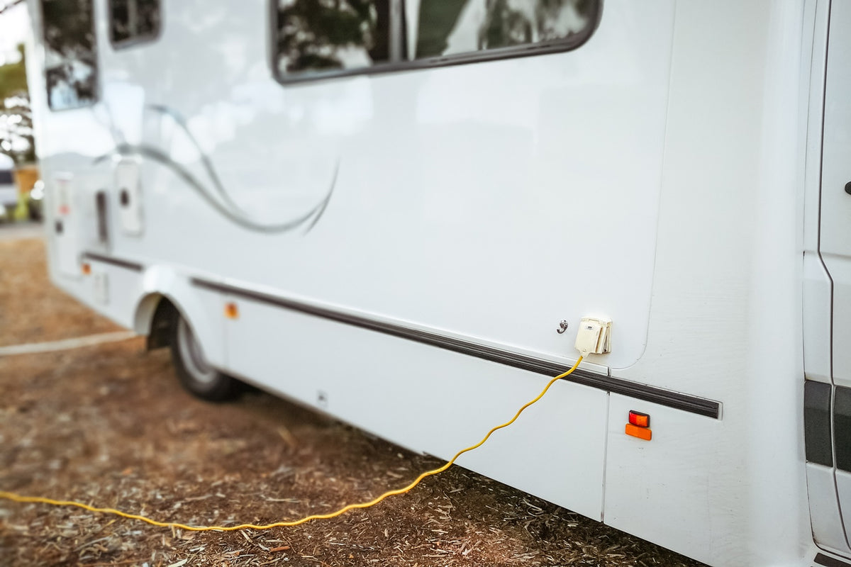 An RVer testing a campground power pedestal with a surge protector before connecting a 30A cord to the trailer.