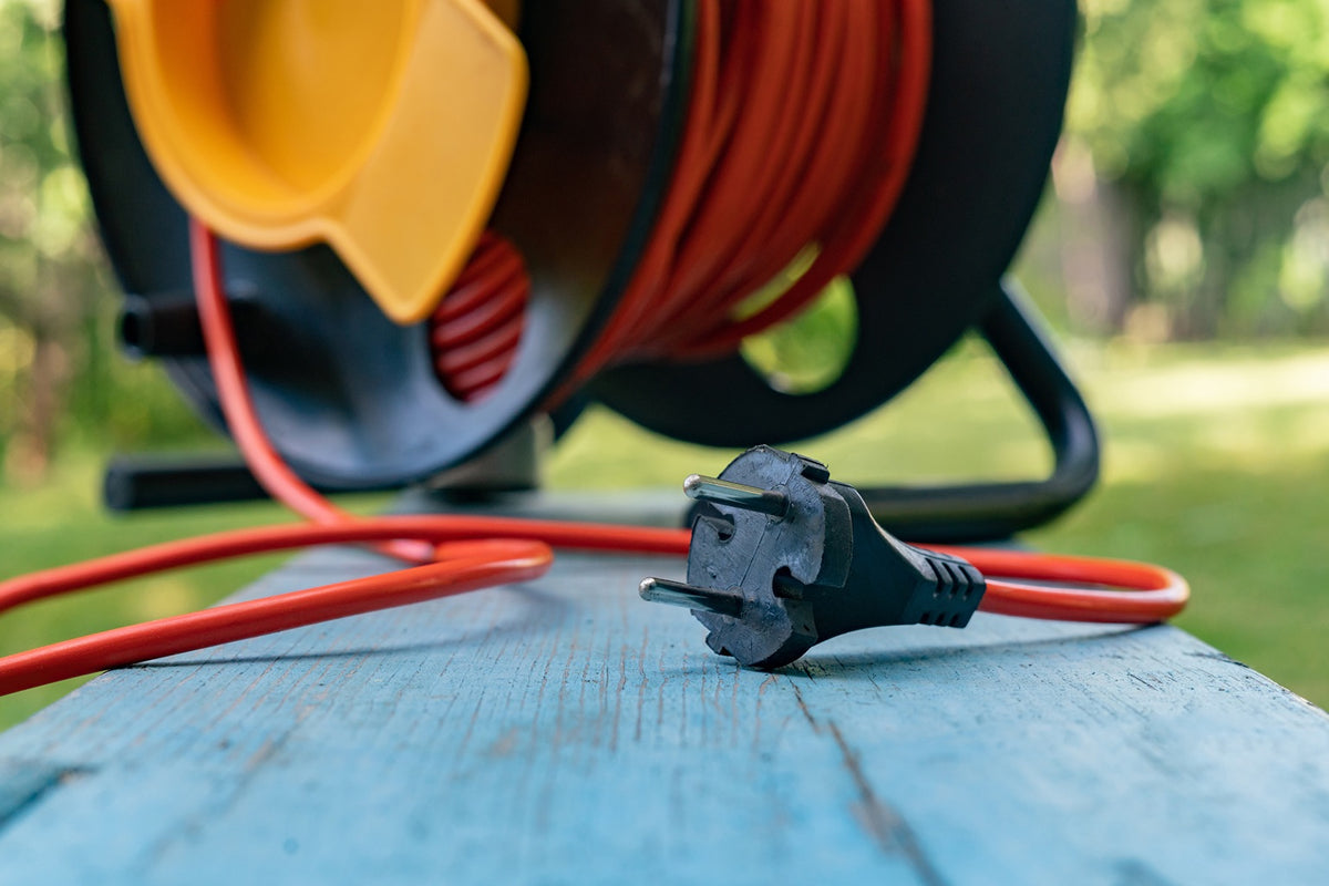 Outdoor-rated extension cords on a jobsite: yellow SJTW and blue SJEOW cords coiled neatly beside a generator after a light rain.