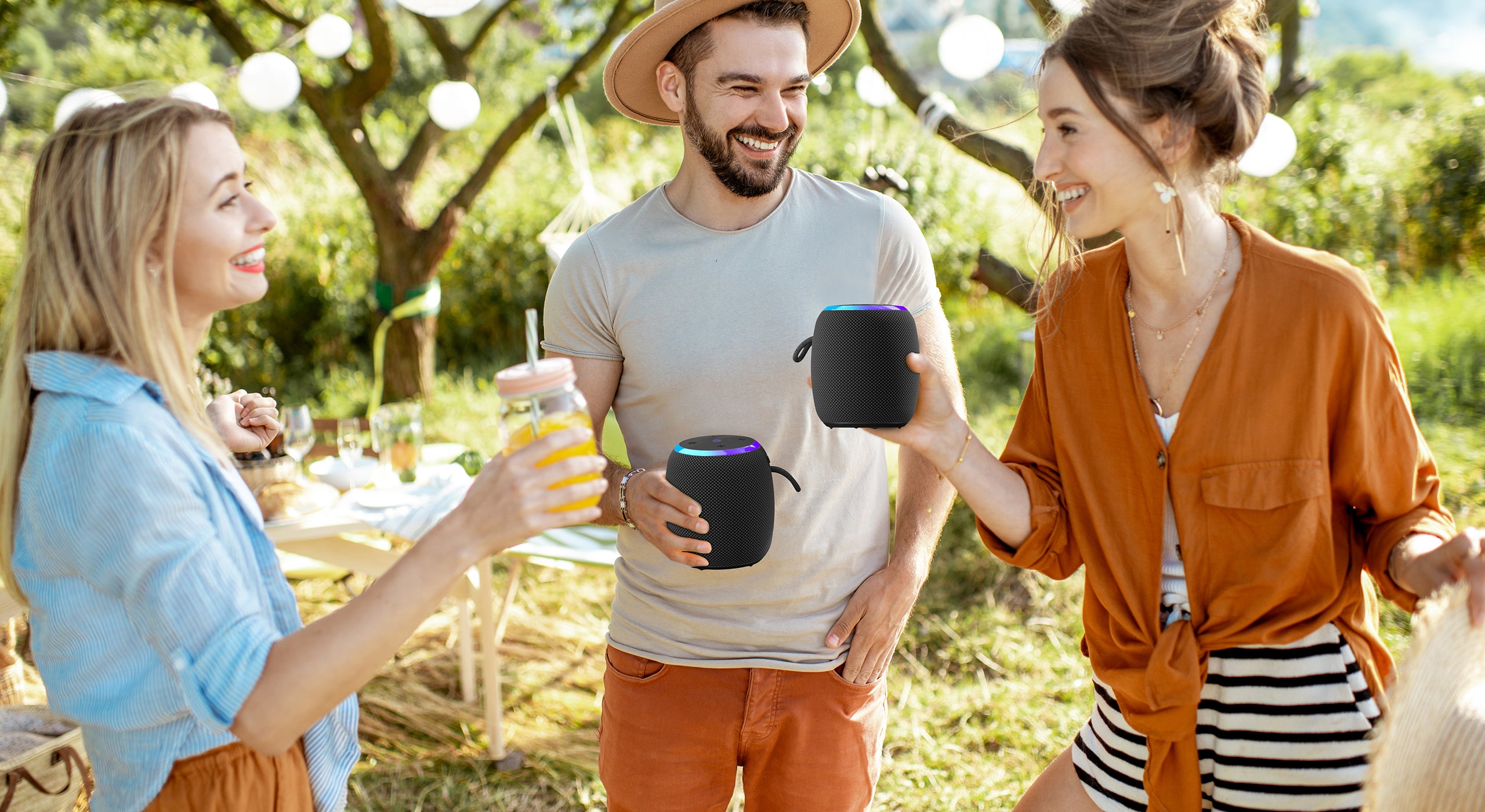 Three friends enjoying a picnic in a park with drinks and a speaker.